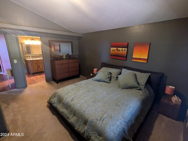 bedroom featuring light colored carpet, lofted ceiling, and ensuite bathroom