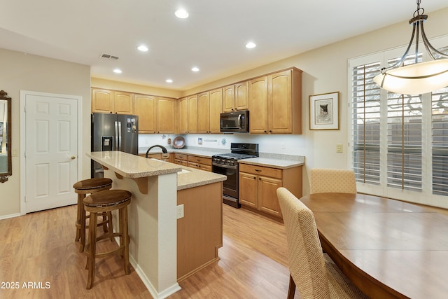 kitchen featuring sink, an island with sink, light hardwood / wood-style floors, pendant lighting, and black appliances