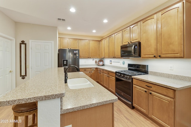 kitchen with a breakfast bar, a kitchen island with sink, black appliances, sink, and light hardwood / wood-style flooring