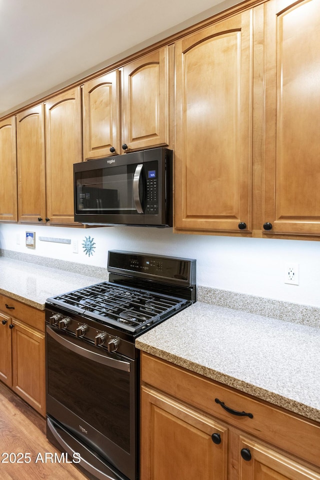 kitchen with black gas range oven, light wood-type flooring, and light stone counters