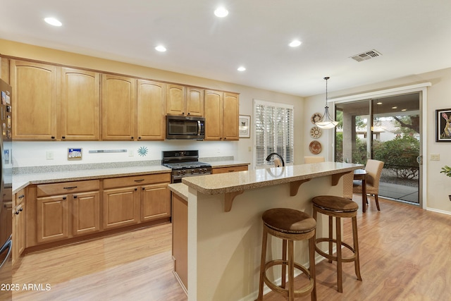 kitchen with black gas range, light hardwood / wood-style floors, decorative light fixtures, and an island with sink