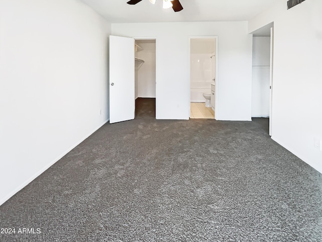 unfurnished bedroom featuring ceiling fan, a spacious closet, dark colored carpet, ensuite bathroom, and a closet