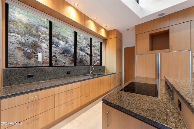 kitchen with light tile patterned flooring, dark stone countertops, sink, and black electric stovetop