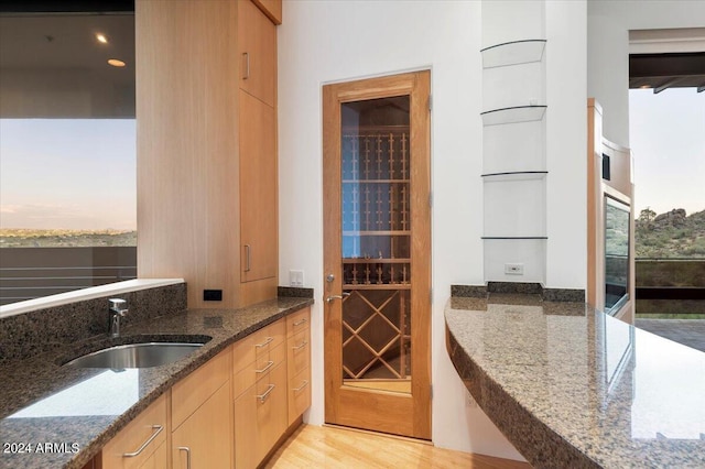 bar with dark stone countertops, sink, and light hardwood / wood-style floors