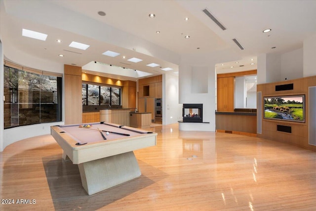 game room with a multi sided fireplace, billiards, light hardwood / wood-style flooring, and a high ceiling