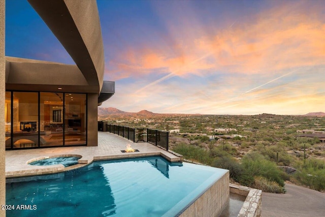 pool at dusk featuring a mountain view, a patio, and an in ground hot tub