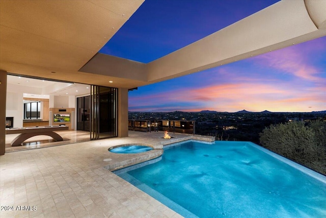 pool at dusk featuring an in ground hot tub and a patio area