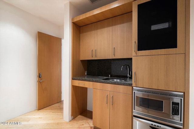 kitchen with tasteful backsplash, light hardwood / wood-style flooring, stainless steel microwave, dark stone countertops, and sink