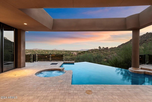 pool at dusk with a mountain view, an in ground hot tub, and a patio area