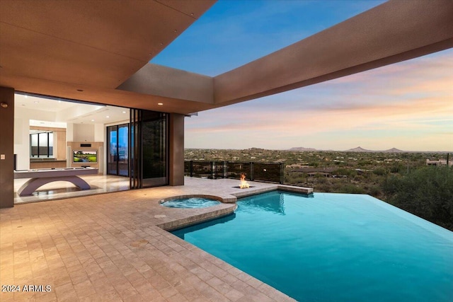 pool at dusk featuring an in ground hot tub, a patio, and a mountain view