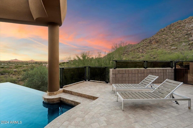 patio terrace at dusk featuring a mountain view and a fenced in pool