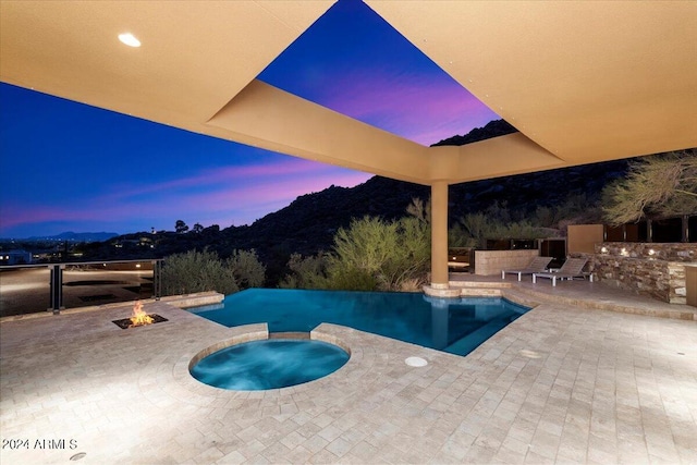 pool at dusk with an in ground hot tub and a patio