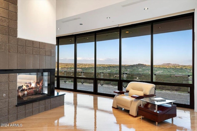 interior space with a mountain view, a tiled fireplace, a wall of windows, light wood-type flooring, and a towering ceiling