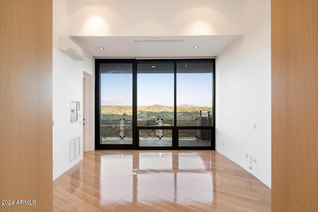 spare room with expansive windows, a wall mounted air conditioner, and light wood-type flooring