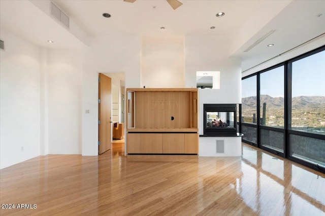 interior space featuring light hardwood / wood-style floors, a wall of windows, a mountain view, a towering ceiling, and a multi sided fireplace