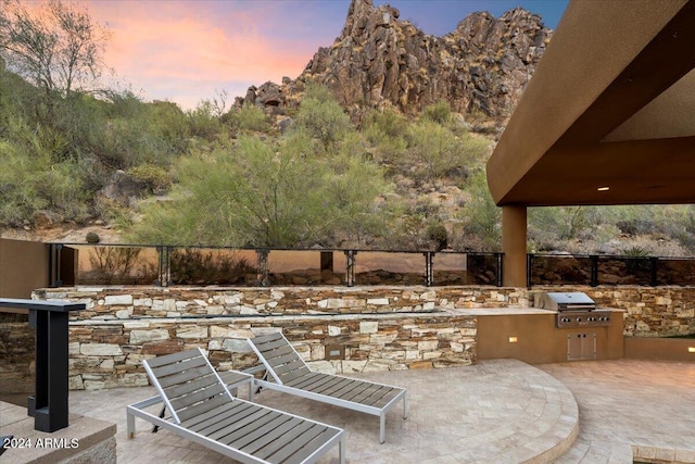 patio terrace at dusk featuring exterior kitchen and grilling area