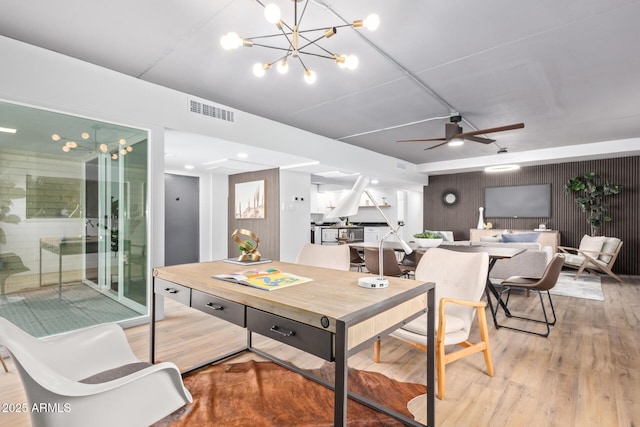 dining area with wooden walls, ceiling fan with notable chandelier, and light hardwood / wood-style floors