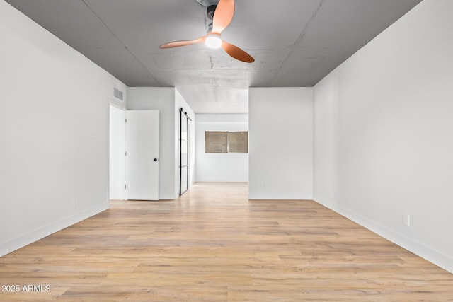 empty room featuring ceiling fan, a barn door, and light wood-type flooring