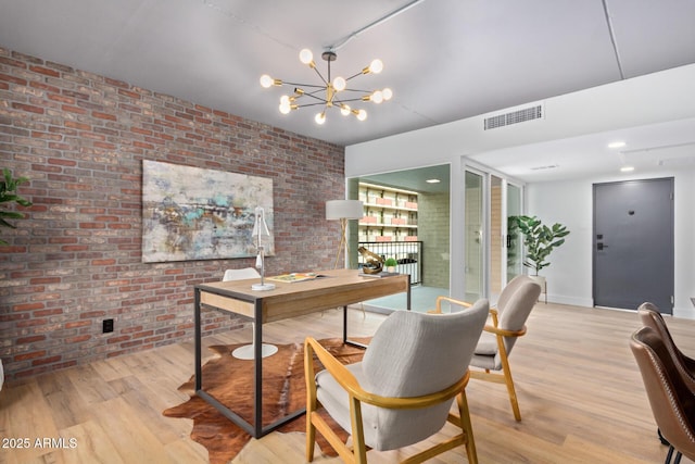 home office featuring brick wall, light hardwood / wood-style flooring, and a chandelier