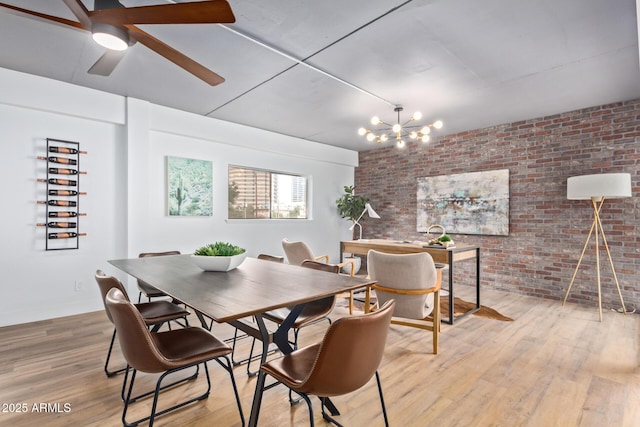 dining area featuring wood-type flooring, brick wall, and ceiling fan with notable chandelier