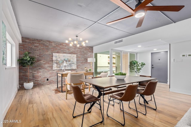 dining space featuring ceiling fan with notable chandelier, brick wall, and light hardwood / wood-style flooring