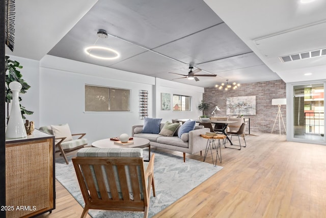 living room with light wood-type flooring, brick wall, and ceiling fan with notable chandelier