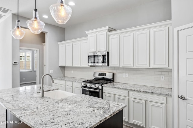 kitchen with stainless steel appliances, a kitchen island with sink, sink, pendant lighting, and white cabinetry