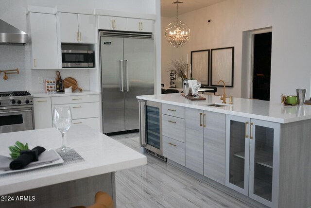 kitchen featuring sink, wall chimney exhaust hood, decorative light fixtures, high quality appliances, and white cabinets