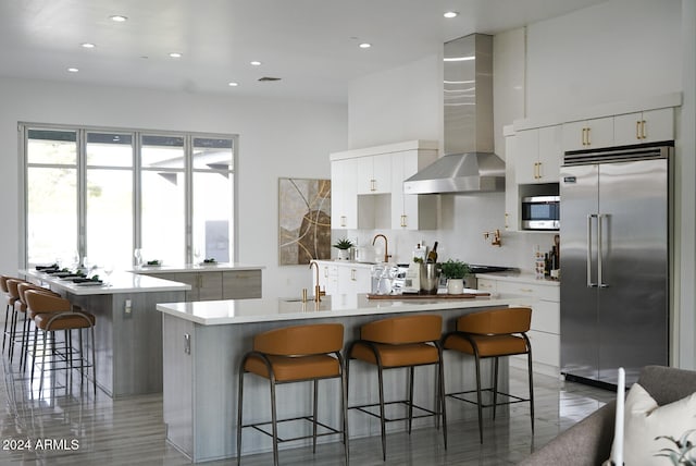 kitchen with stainless steel appliances, wall chimney range hood, a kitchen island, a breakfast bar area, and white cabinets