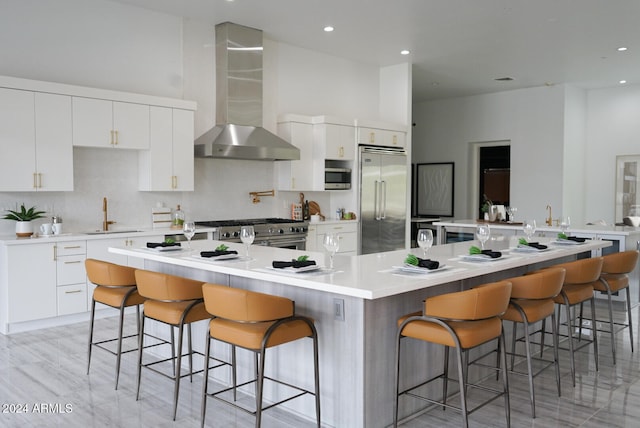 kitchen with white cabinets, high end appliances, a spacious island, and wall chimney range hood