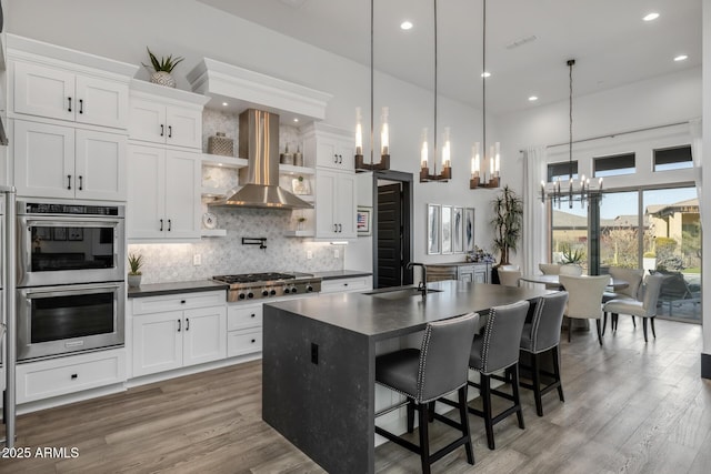 kitchen featuring sink, white cabinetry, stainless steel appliances, a kitchen island with sink, and exhaust hood