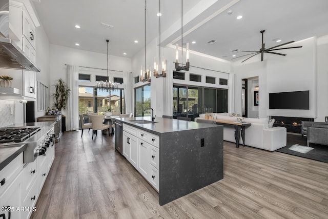 kitchen with sink, a kitchen island with sink, stainless steel appliances, decorative light fixtures, and wall chimney exhaust hood