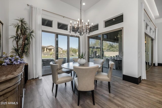 dining space featuring dark wood-type flooring, a towering ceiling, and a notable chandelier