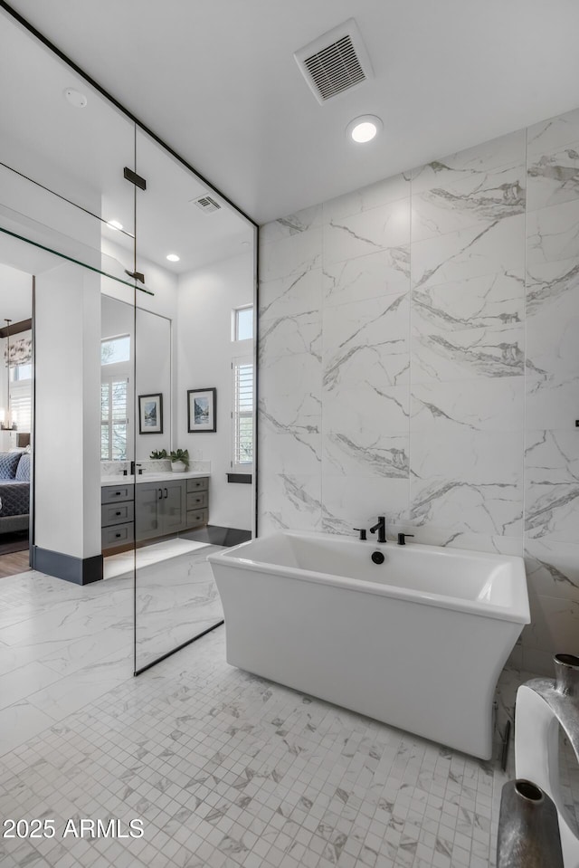 bathroom featuring vanity, a bath, and tile walls