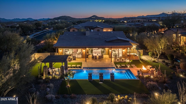 back house at dusk with a mountain view, outdoor lounge area, a patio, and an outdoor kitchen