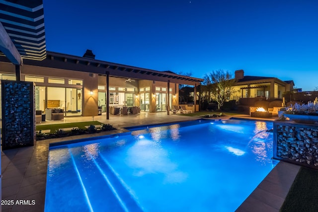 pool at dusk with pool water feature, an outdoor living space with a fire pit, ceiling fan, and a patio area