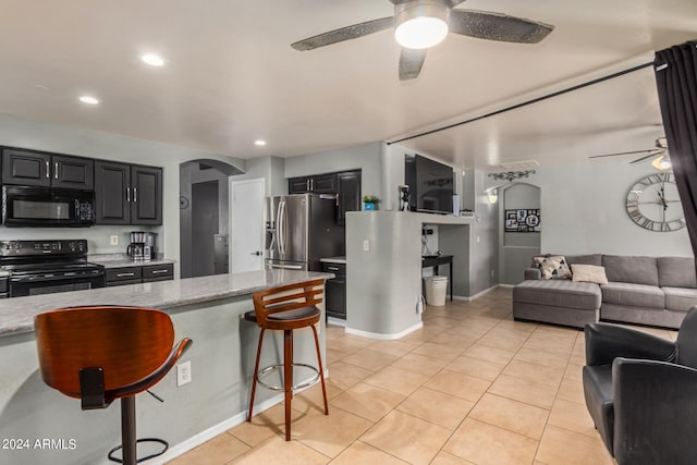 kitchen with black appliances, light stone counters, a kitchen bar, and ceiling fan