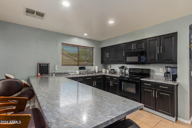 kitchen featuring black appliances, a breakfast bar area, light tile patterned floors, and kitchen peninsula