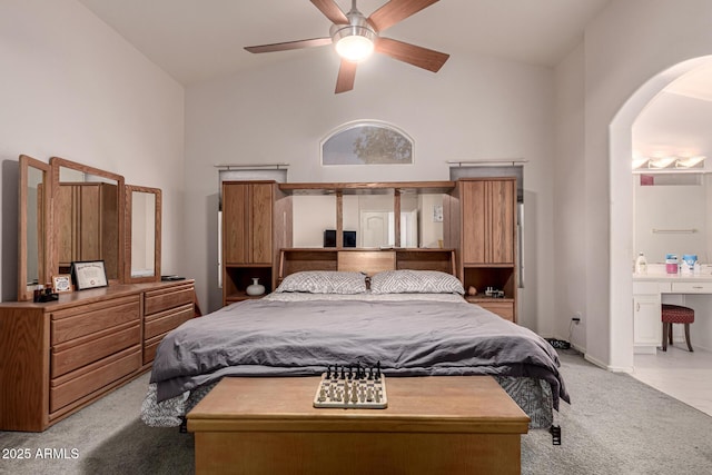 bedroom featuring a ceiling fan, carpet flooring, arched walkways, ensuite bath, and vaulted ceiling