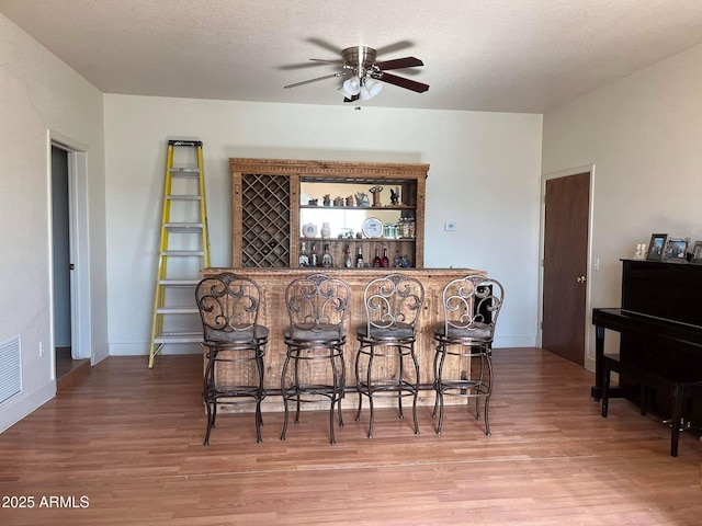 bar with light wood-type flooring, a ceiling fan, baseboards, and a bar