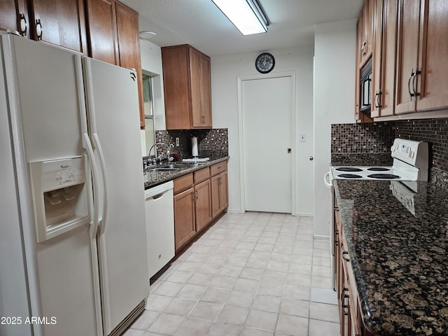 kitchen with tasteful backsplash, brown cabinets, a sink, dark stone countertops, and white appliances