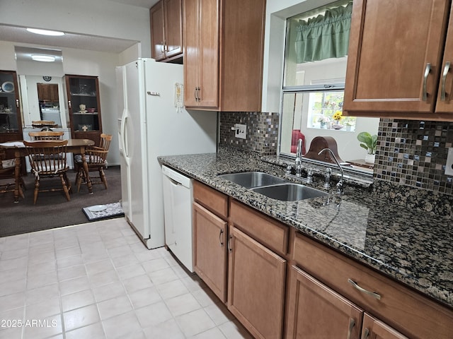 kitchen featuring brown cabinets, a sink, dishwasher, dark stone counters, and decorative backsplash