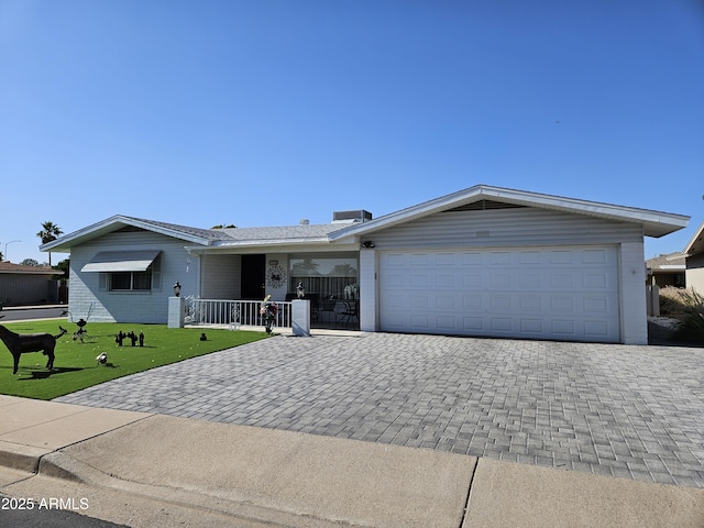 single story home with covered porch, decorative driveway, an attached garage, and a front yard