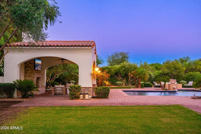 pool at dusk featuring a patio area, pool water feature, and a lawn