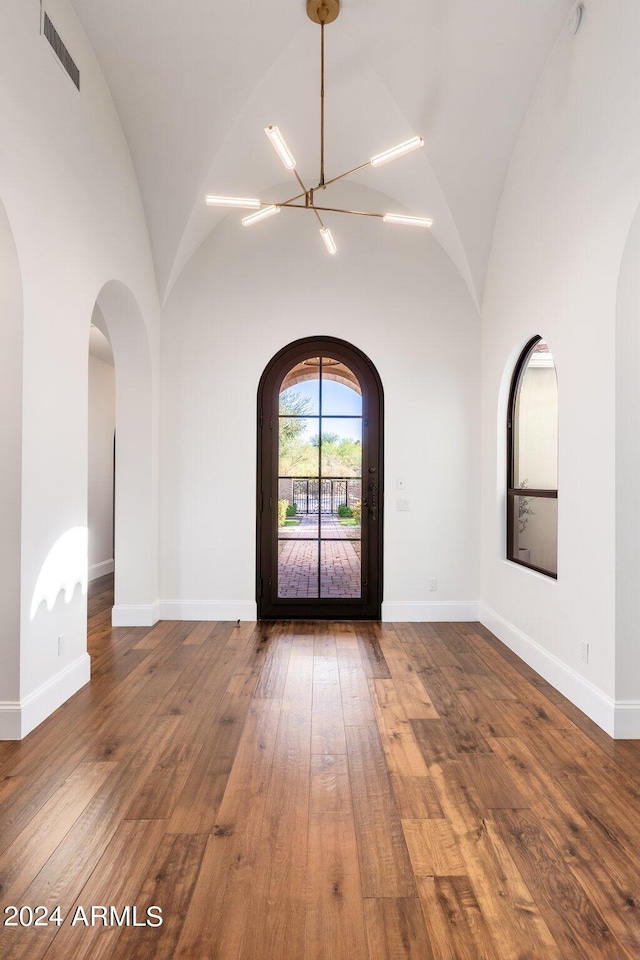 unfurnished room with high vaulted ceiling, a chandelier, and hardwood / wood-style floors