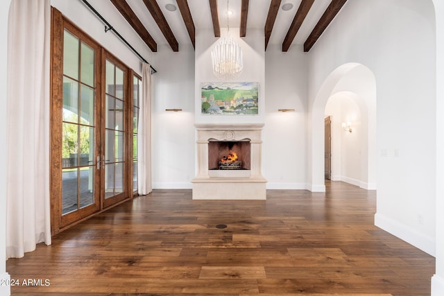 unfurnished living room with dark wood-type flooring, beamed ceiling, an inviting chandelier, and french doors