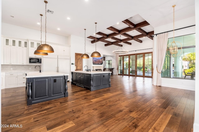 kitchen with hanging light fixtures, dark hardwood / wood-style flooring, white cabinetry, a kitchen island with sink, and built in appliances