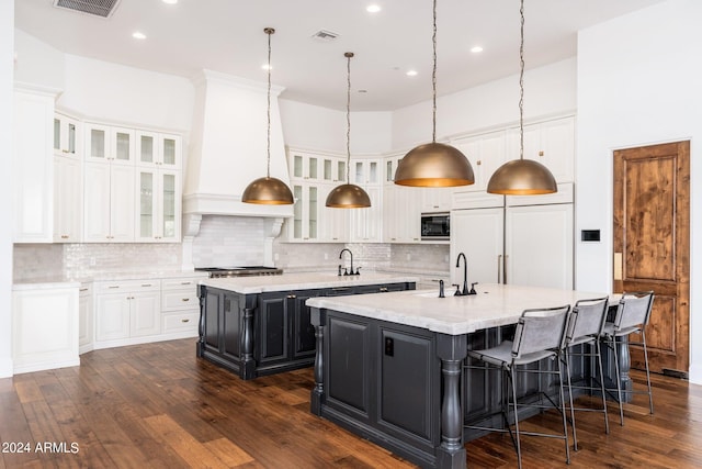 kitchen featuring a large island with sink, dark hardwood / wood-style flooring, hanging light fixtures, built in appliances, and decorative backsplash