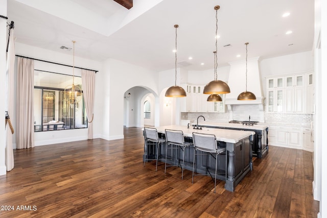 kitchen with a center island with sink, decorative light fixtures, dark hardwood / wood-style floors, and white cabinets