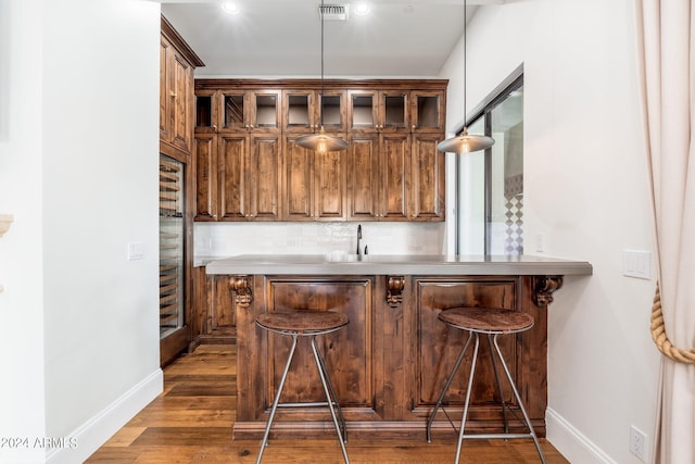 bar featuring dark wood-type flooring, backsplash, sink, and hanging light fixtures